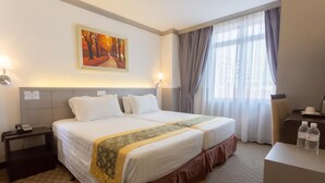 Een hotelkamer met twee bedden, een schilderij aan de muur, een nachtkastje met een telefoon en een bureau met waterflesjes.