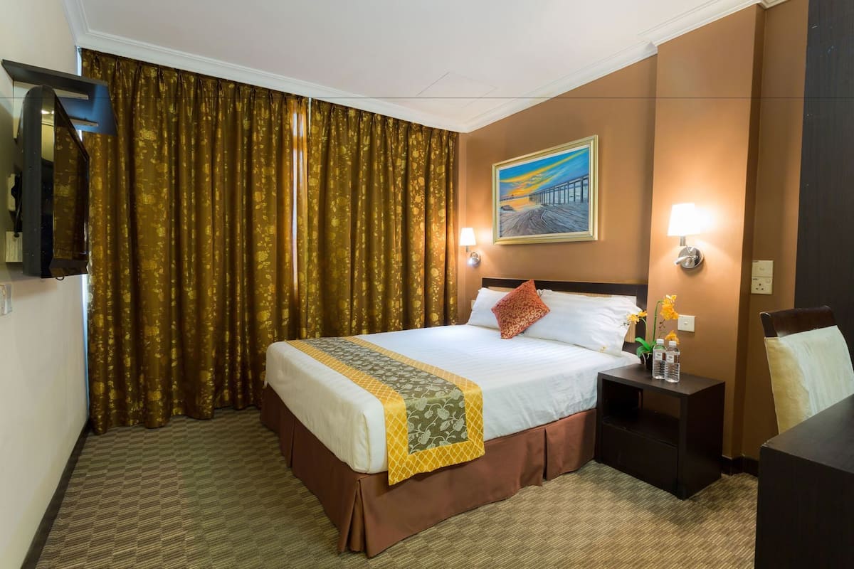 A hotel room with a bed, a nightstand, a lamp, a painting on the wall, and a window with curtains.