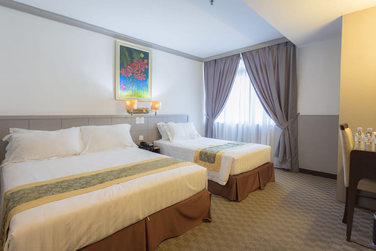 A hotel room with two beds, a painting on the wall, a desk with a chair, and a window with curtains.