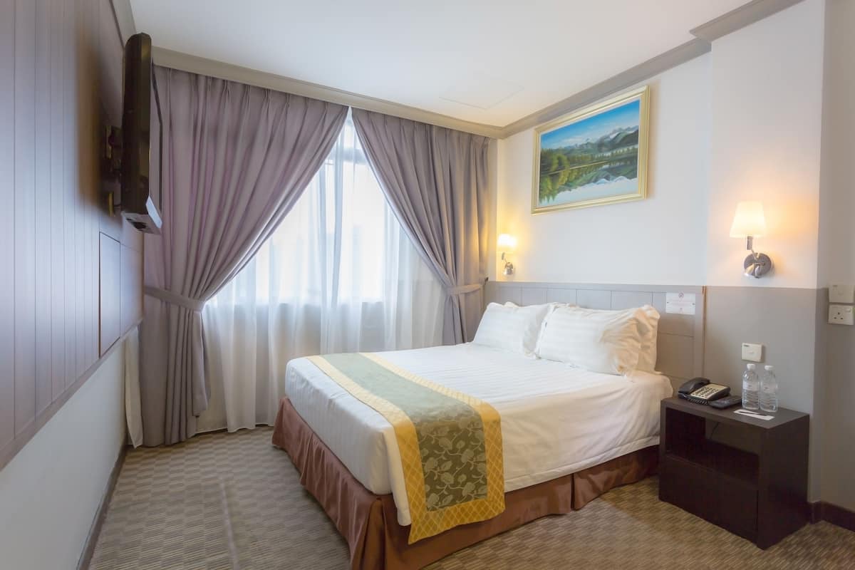 A hotel room with a bed, a nightstand, a painting on the wall, and a window with curtains.