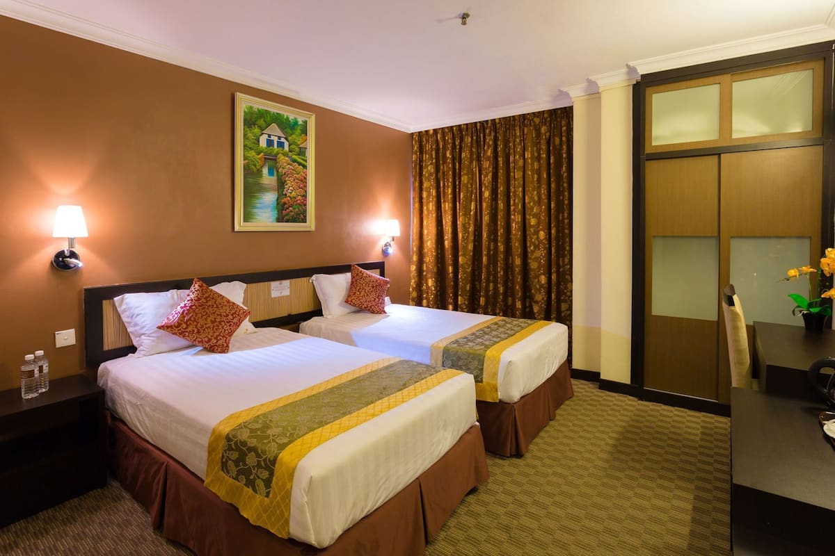 A hotel room with two beds, a painting on the wall, a desk with a chair, and a view of a building through a window.