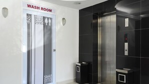 Een moderne badkamer met een glazen deur, een zwart betegelde muur en een digitaal bedieningspaneel voor de lift.