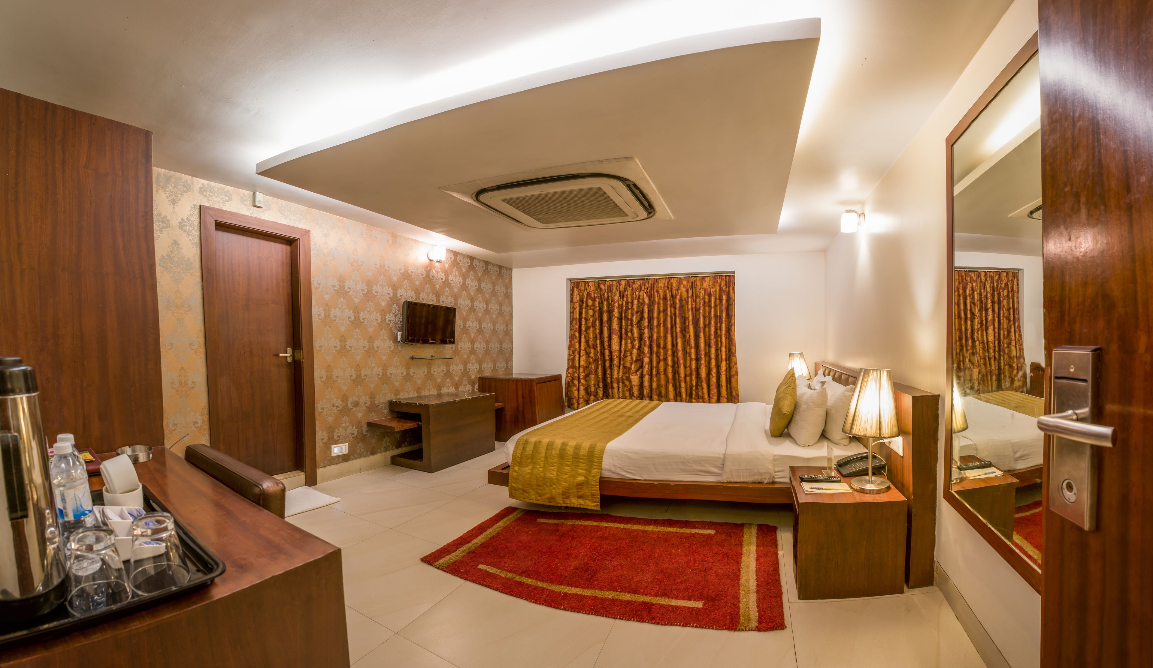 Habitación de hotel con cama, mesita de noche, espejo, escritorio y una alfombra roja.