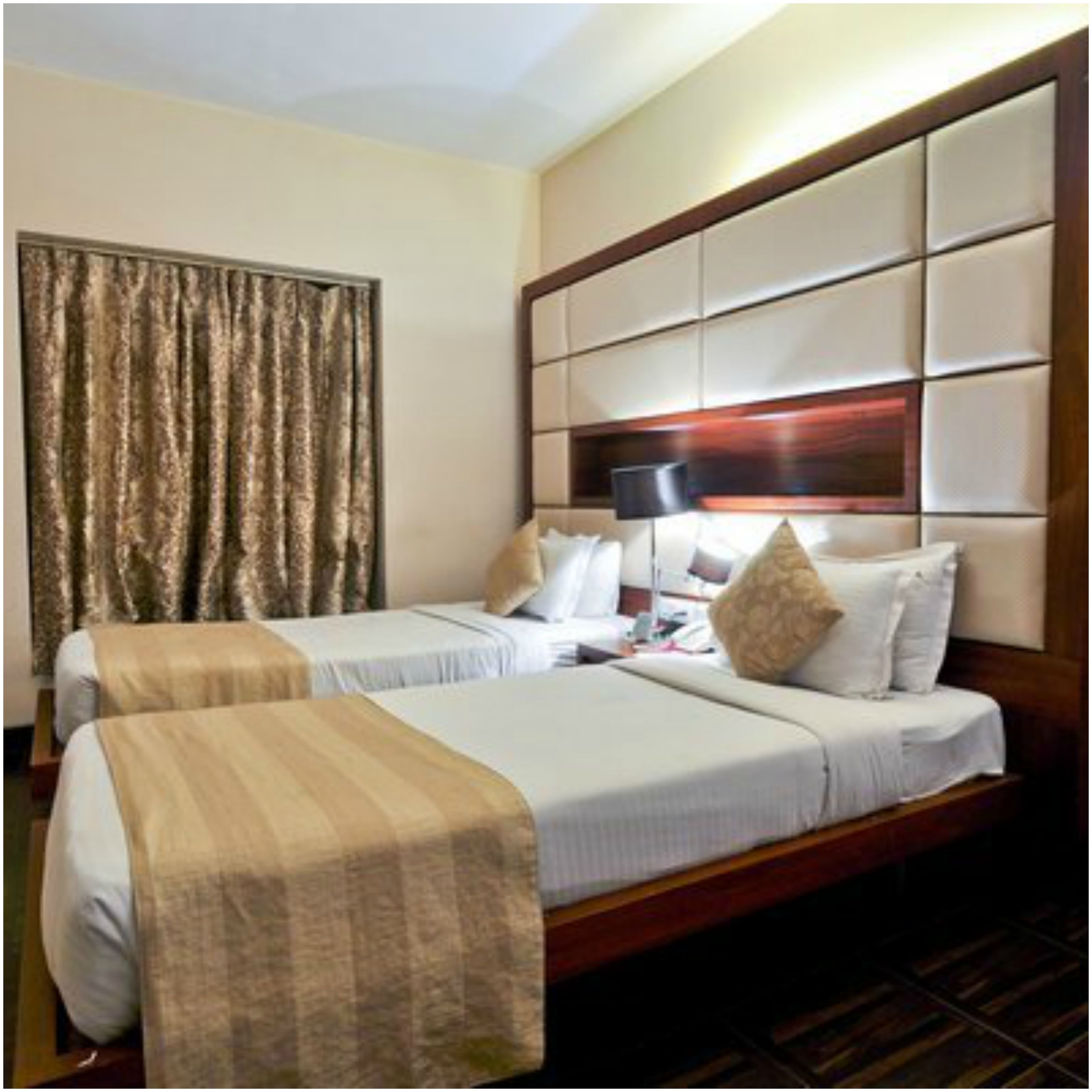 A hotel room with two beds, a large window with curtains, a wooden headboard, and a bedside table with a lamp.
