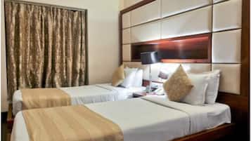 A hotel room with two beds, a large window with curtains, a wooden headboard, and a bedside table with a lamp.