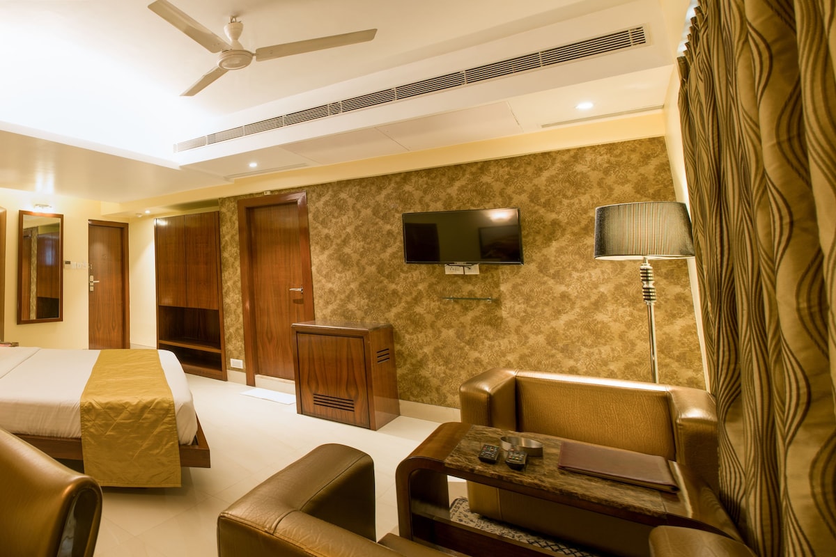 A hotel room with a bed, two sofas, a TV, a desk, and a ceiling fan.