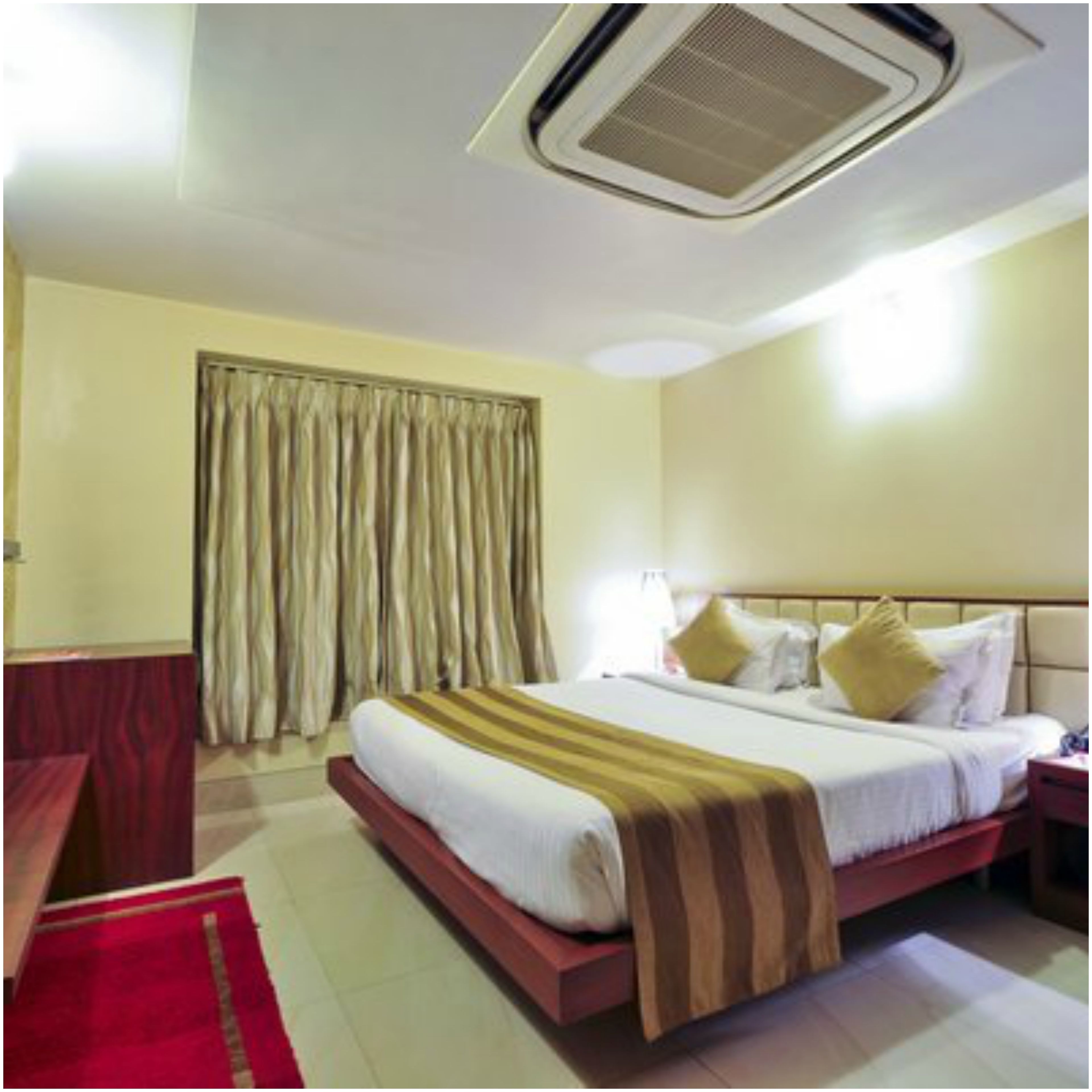 A hotel room with a bed, a nightstand, a desk, a chair, and a window with curtains.