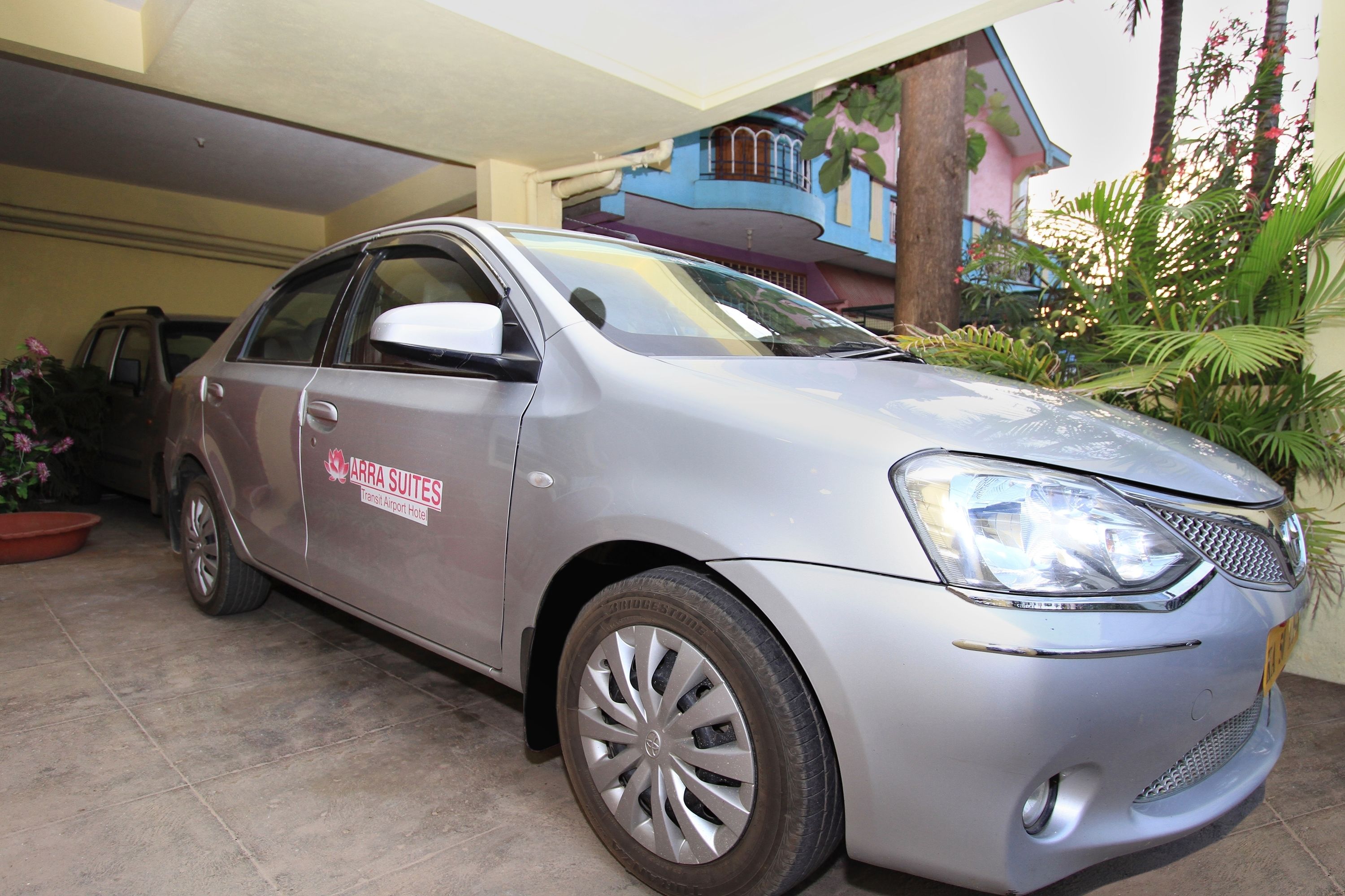 A silver car parked in a garage with a sign on the side that reads "ARRA SUITES Transit Airport Hotel."