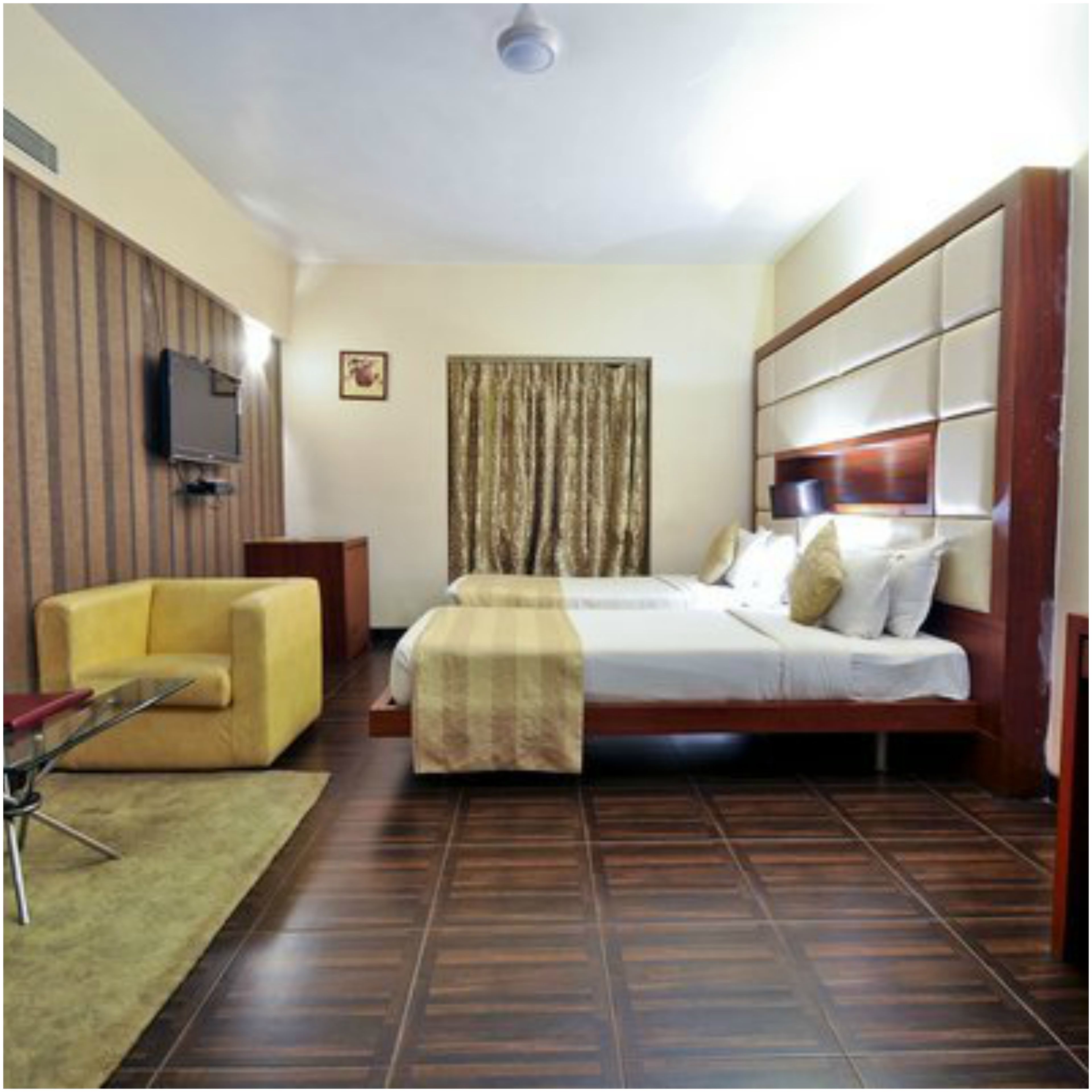 Una habitación de hotel con cama, sofá, televisor montado en la pared y ventana con cortinas.