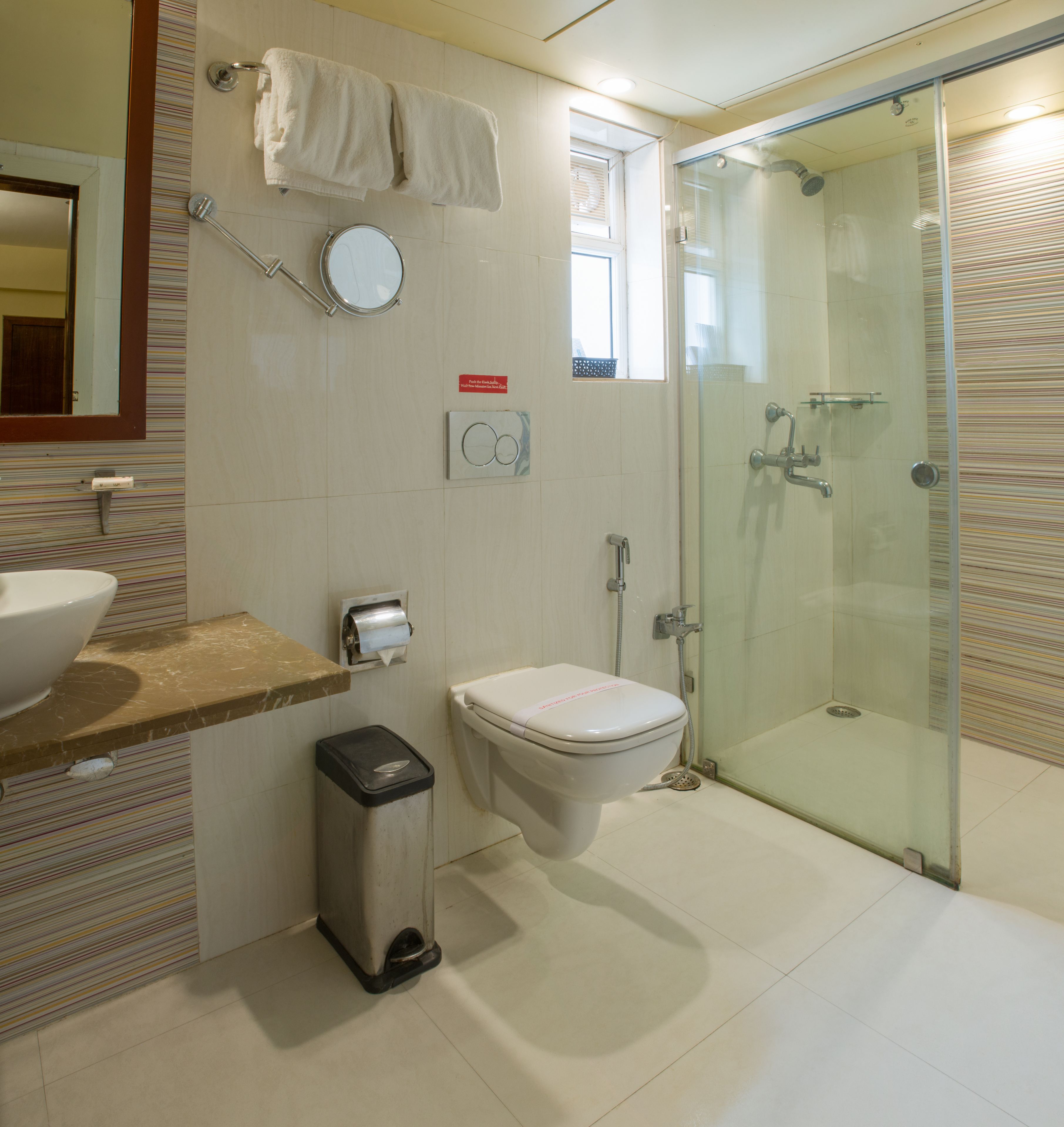 A modern bathroom with a glass-enclosed shower, a toilet, a sink, and a trash bin.