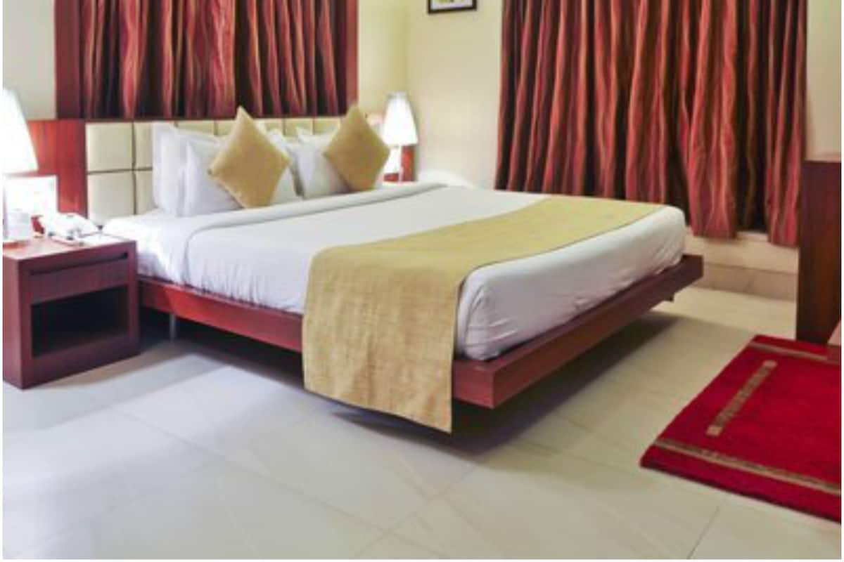 A hotel room with a large bed, two bedside tables with lamps, a red carpet, and heavy curtains.