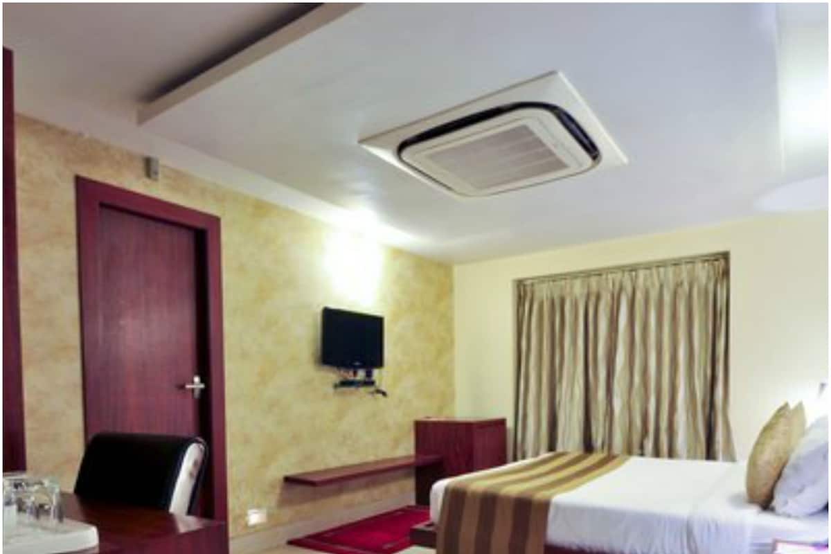 A hotel room with a bed, a desk with a chair, a television, and a window with curtains.