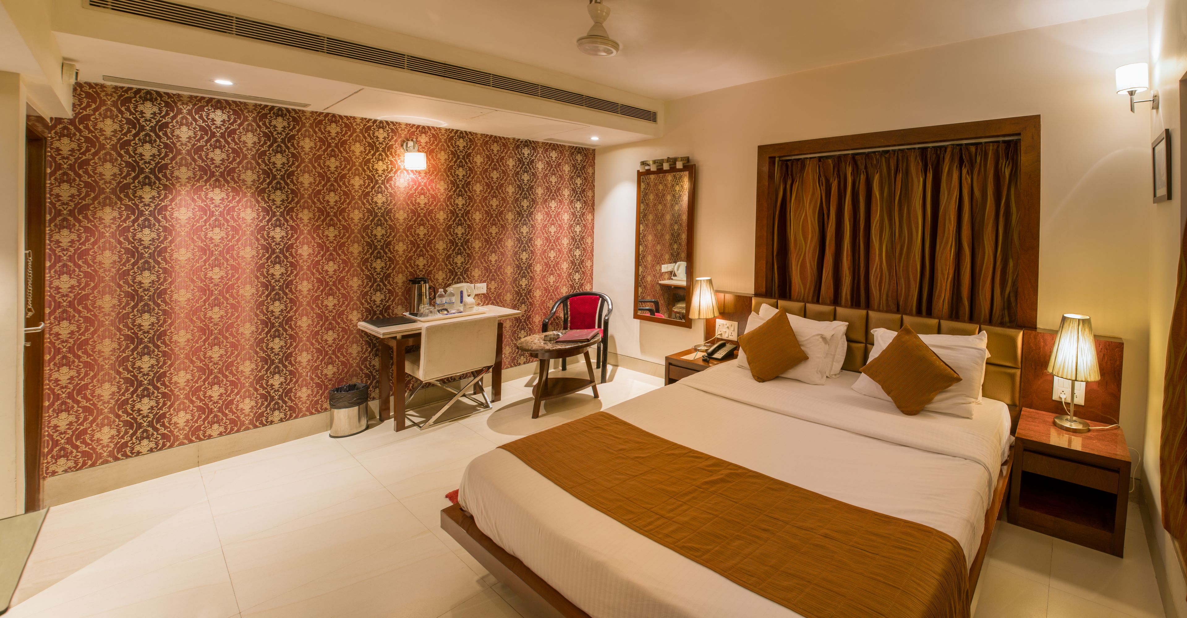 Une chambre d’hôtel avec un grand lit, un bureau et une chaise. On y trouve une table de chevet avec une lampe et un téléphone.