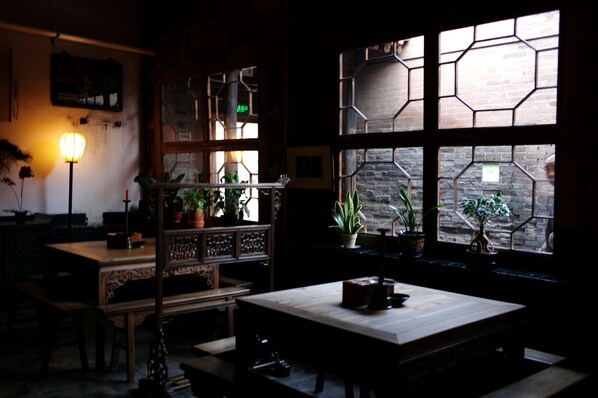 A dimly lit room with a wooden table, a bench, and a shelf with potted plants. - Yide Hotel (Jinzhong)