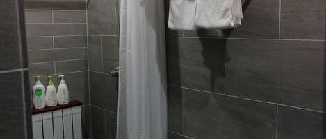 A modern bathroom with grey tiles, a shower curtain, a towel rack, and three bottles of toiletries on a shelf.