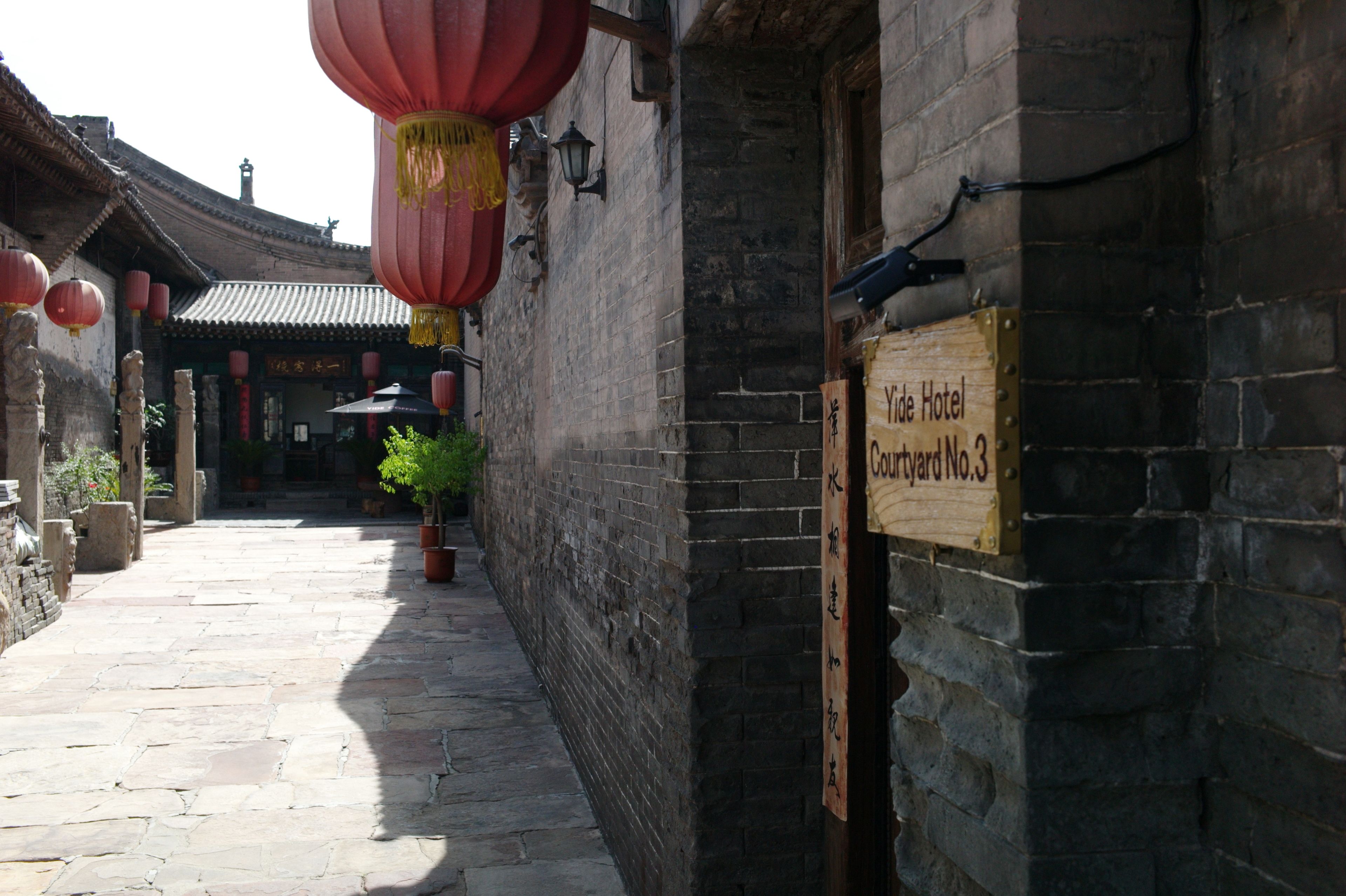 A narrow alleyway with traditional architecture, a wooden sign indicating 'Yade Hotel Courtyard No.3', and red lanterns.