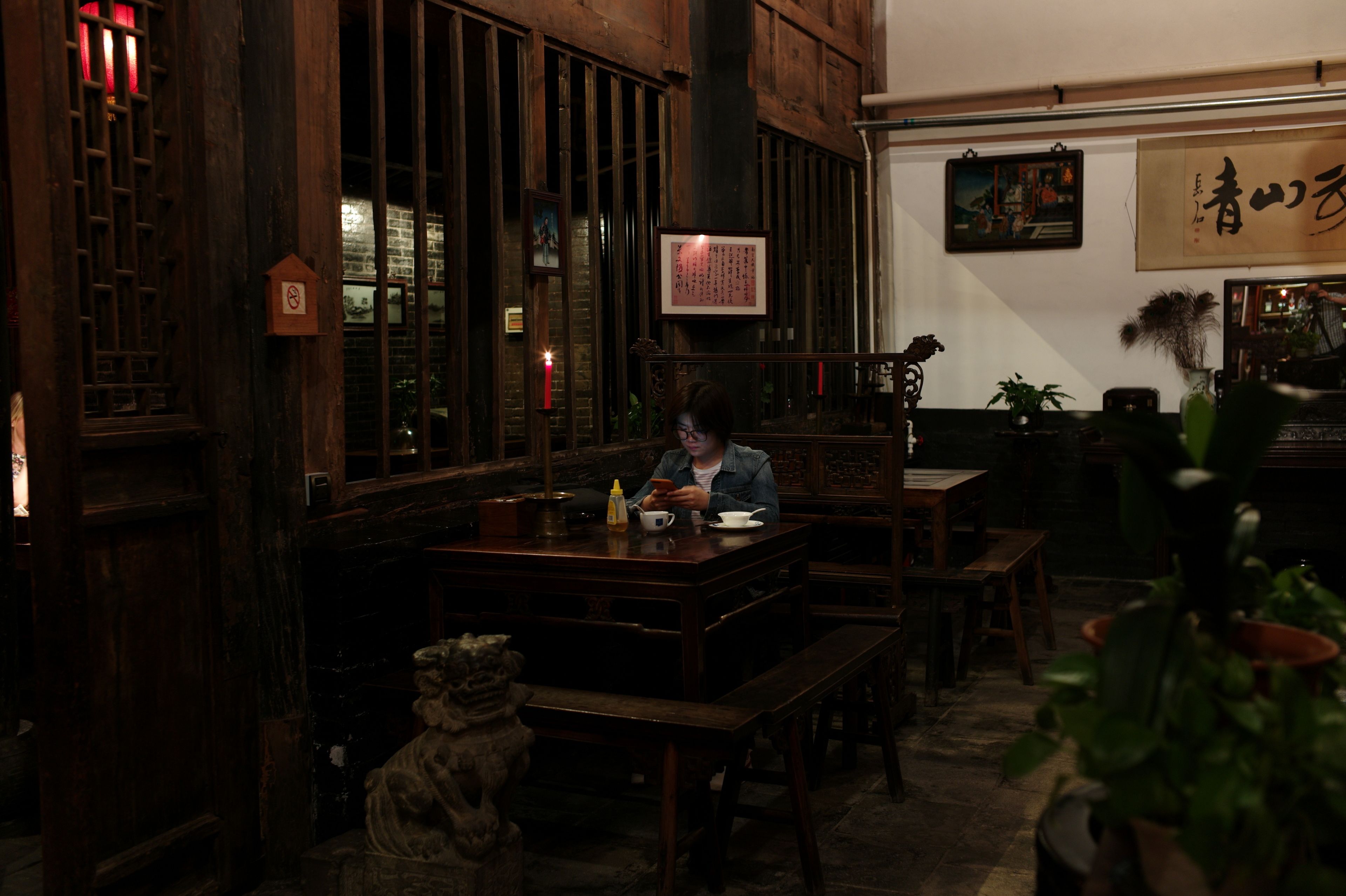 Interior de madera tradicional con una persona sentada en una mesa, muebles de madera y una estatua.