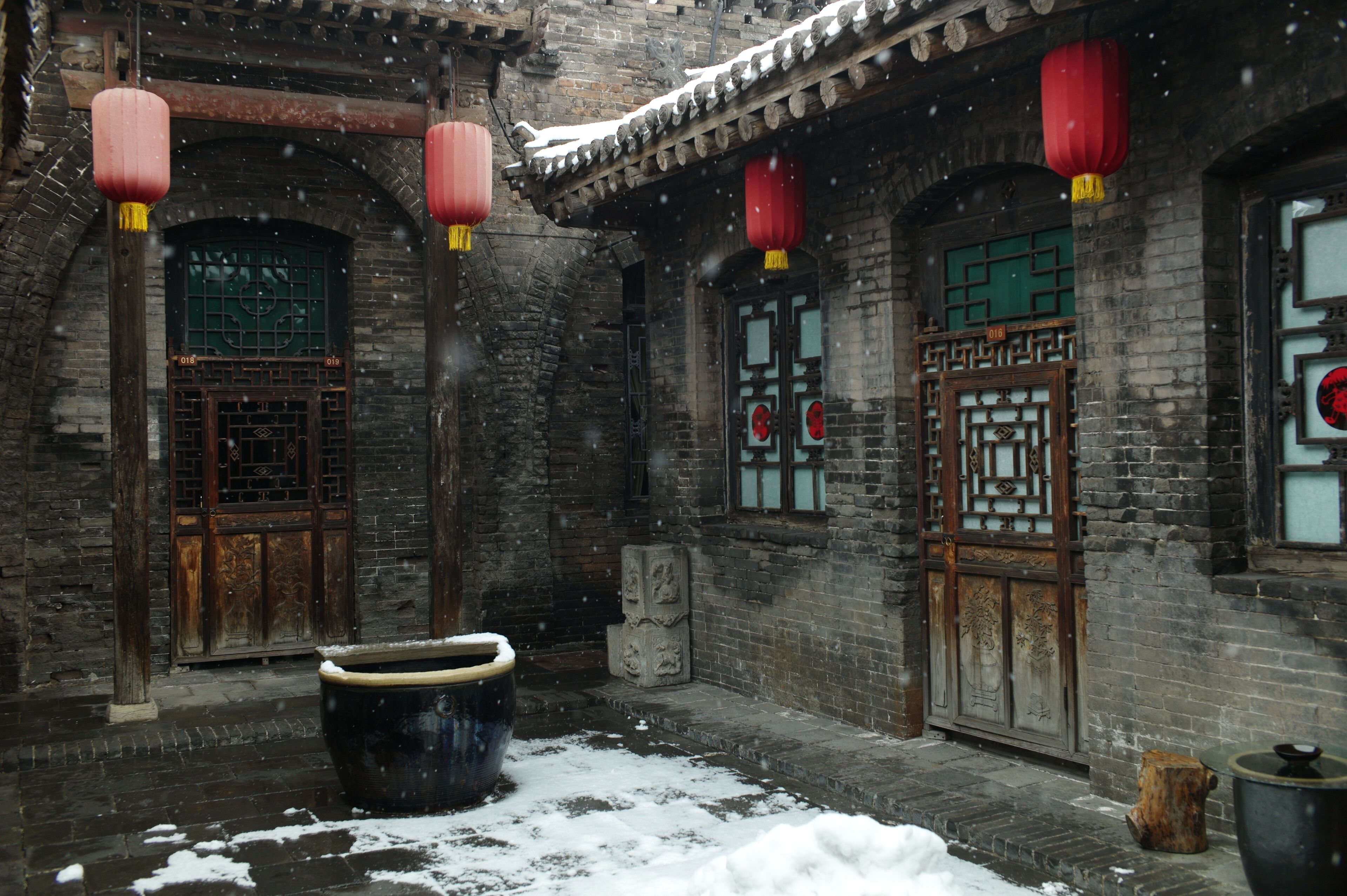 A traditional courtyard with brick walls, wooden doors, and red lanterns.