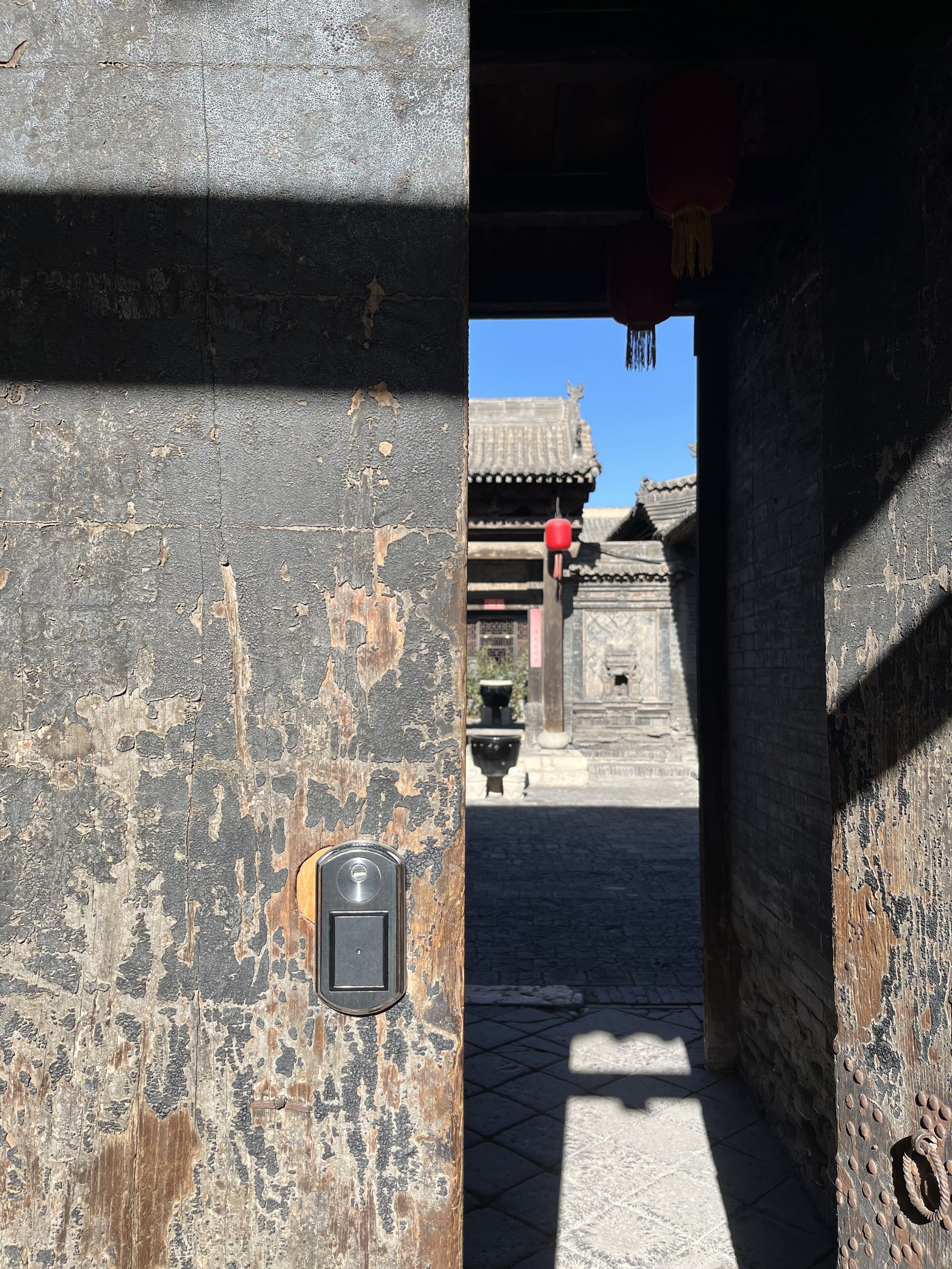 A weathered stone wall with a metal door and a traditional red lantern.
