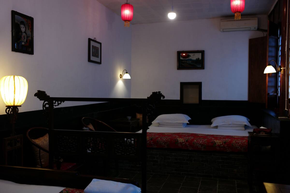 A traditional room with a bed, a chair, a wall-mounted shelf, and a hanging red lantern.
