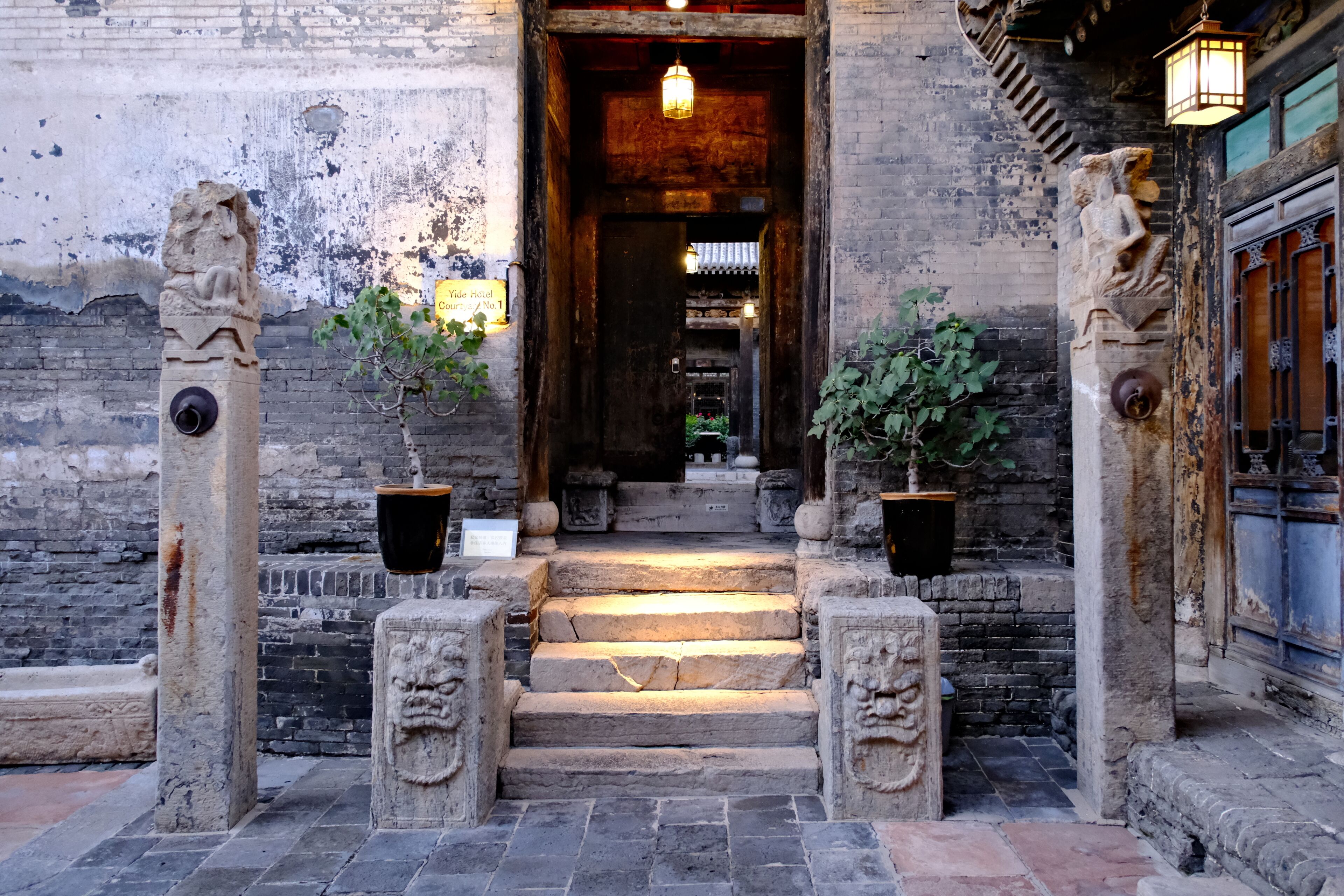 A traditional building entrance with stone lions, potted plants, and a sign indicating a hotel.