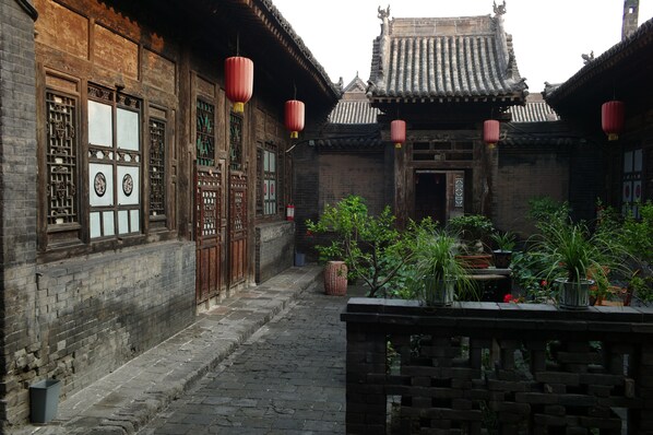 Stroll through this serene courtyard, surrounded by a traditional building with a tiled roof and decorative elements, featuring a fountain and lush greenery.