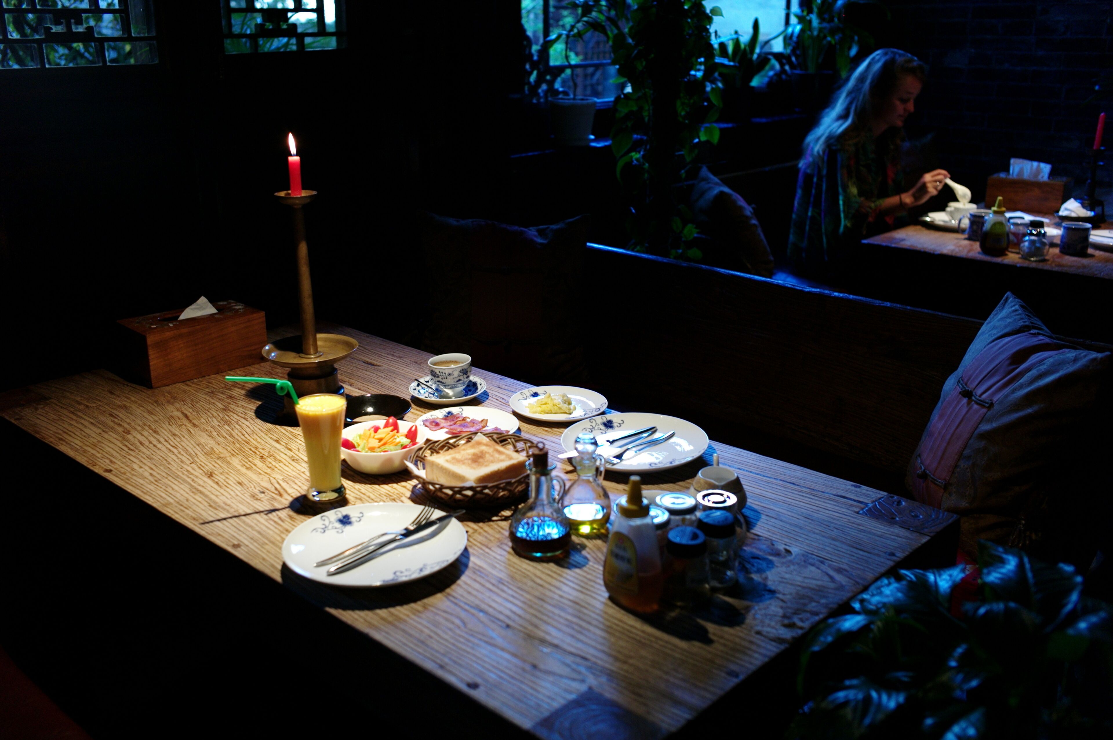 Un'area ristorazione scarsamente illuminata, con un tavolo in legno apparecchiato per un pasto, una candela e diversi piatti.