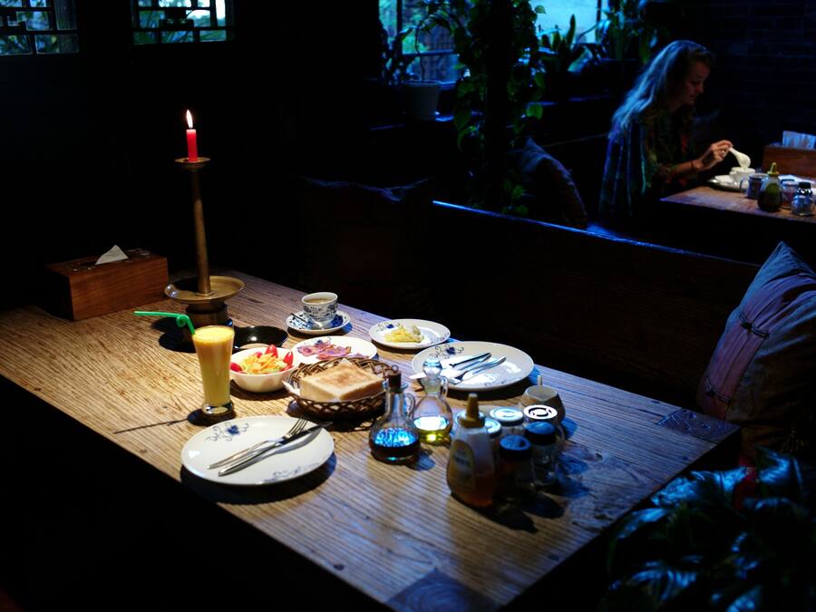 Comedor tenuemente iluminado con una mesa de madera dispuesta para una comida, una vela y diversos platos.