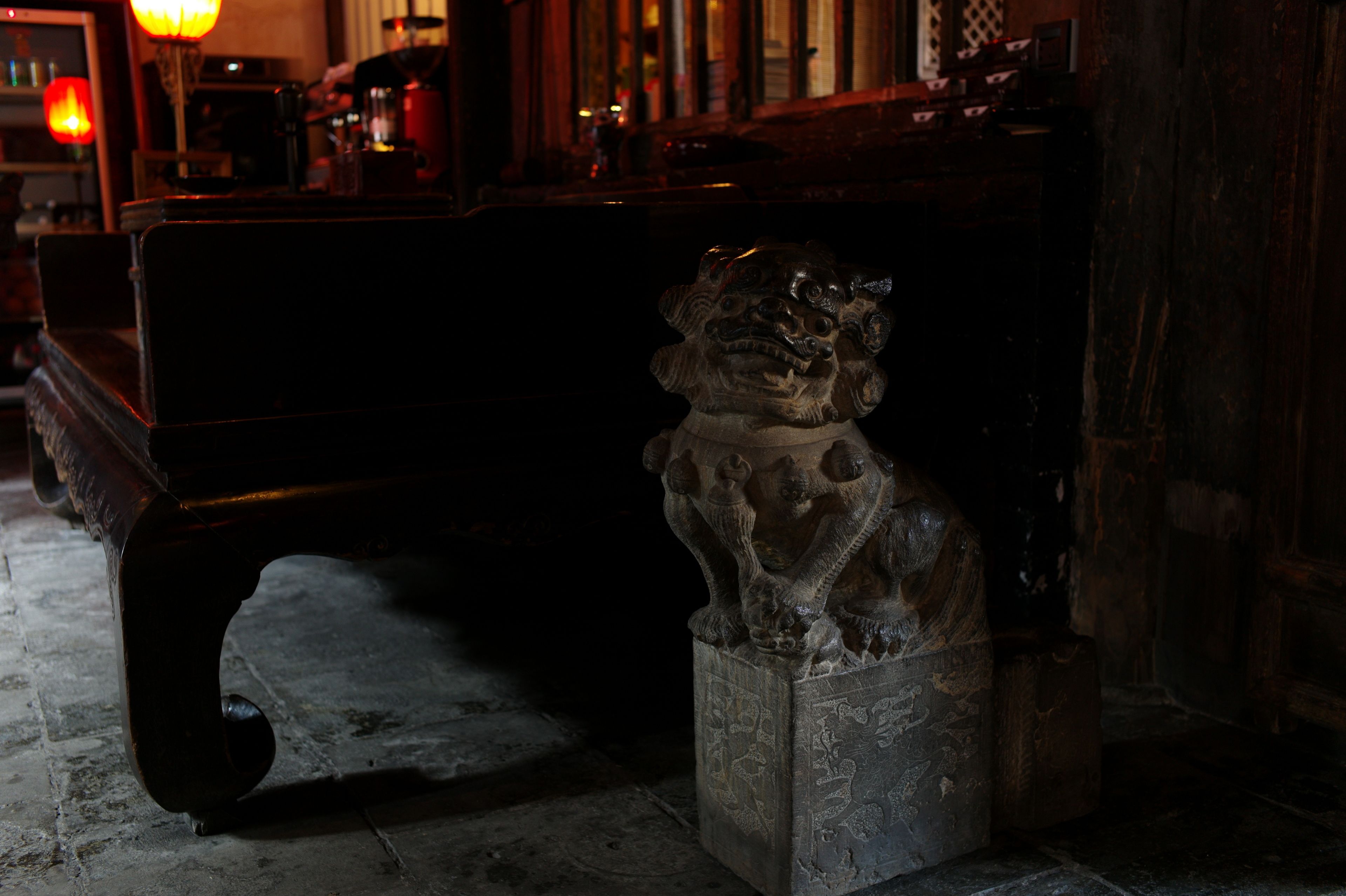A stone lion statue in a dimly lit room with a wooden bench and a table in the background.
