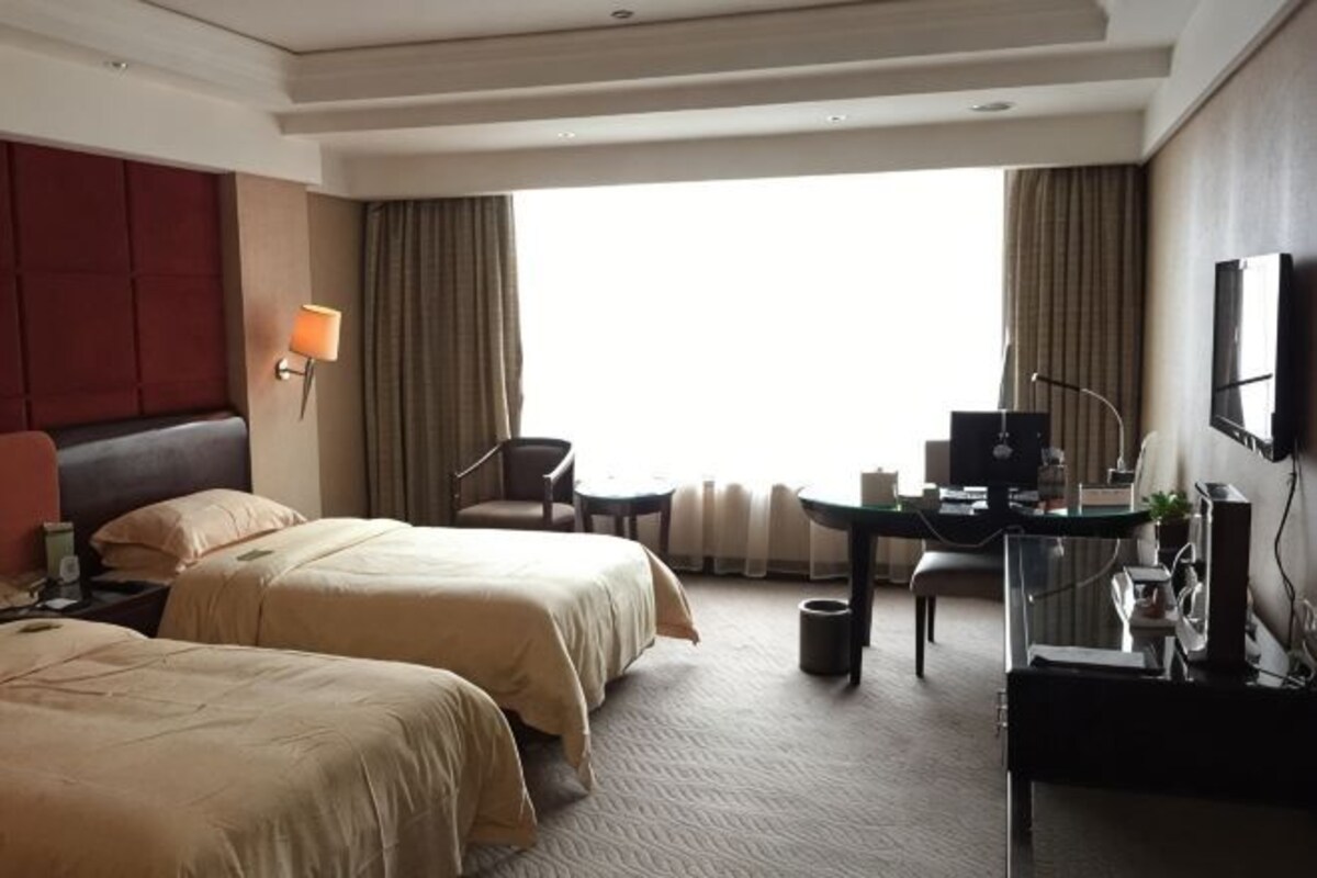 A hotel room with two beds, a desk, a chair, a lamp, and a large window.