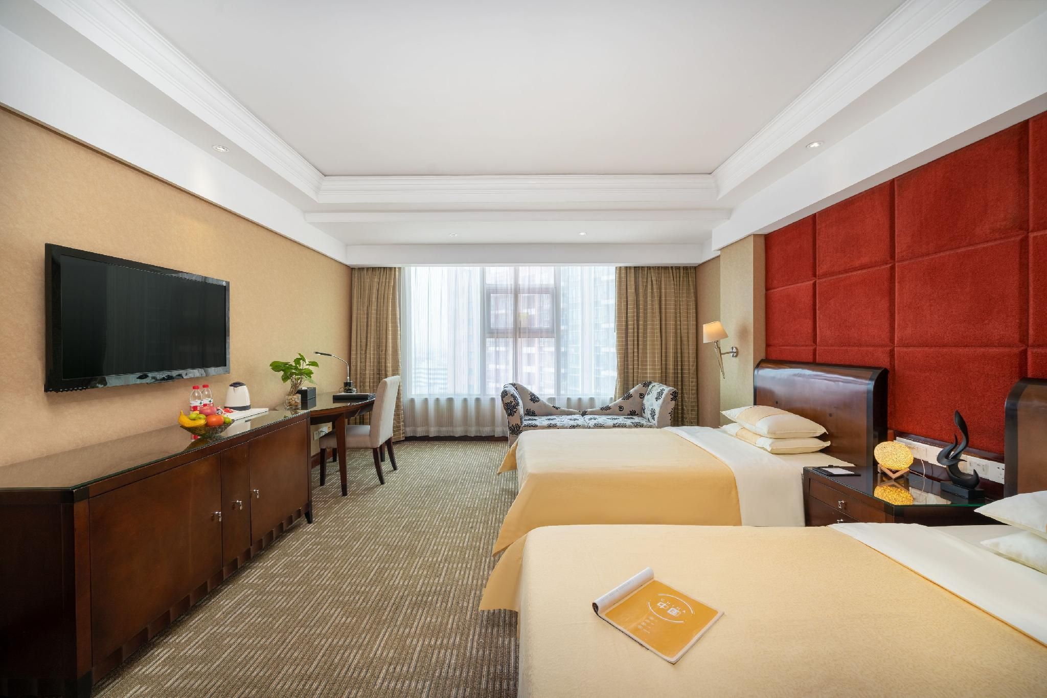A hotel room with a bed, a desk, a chair, a television, and a window with curtains.