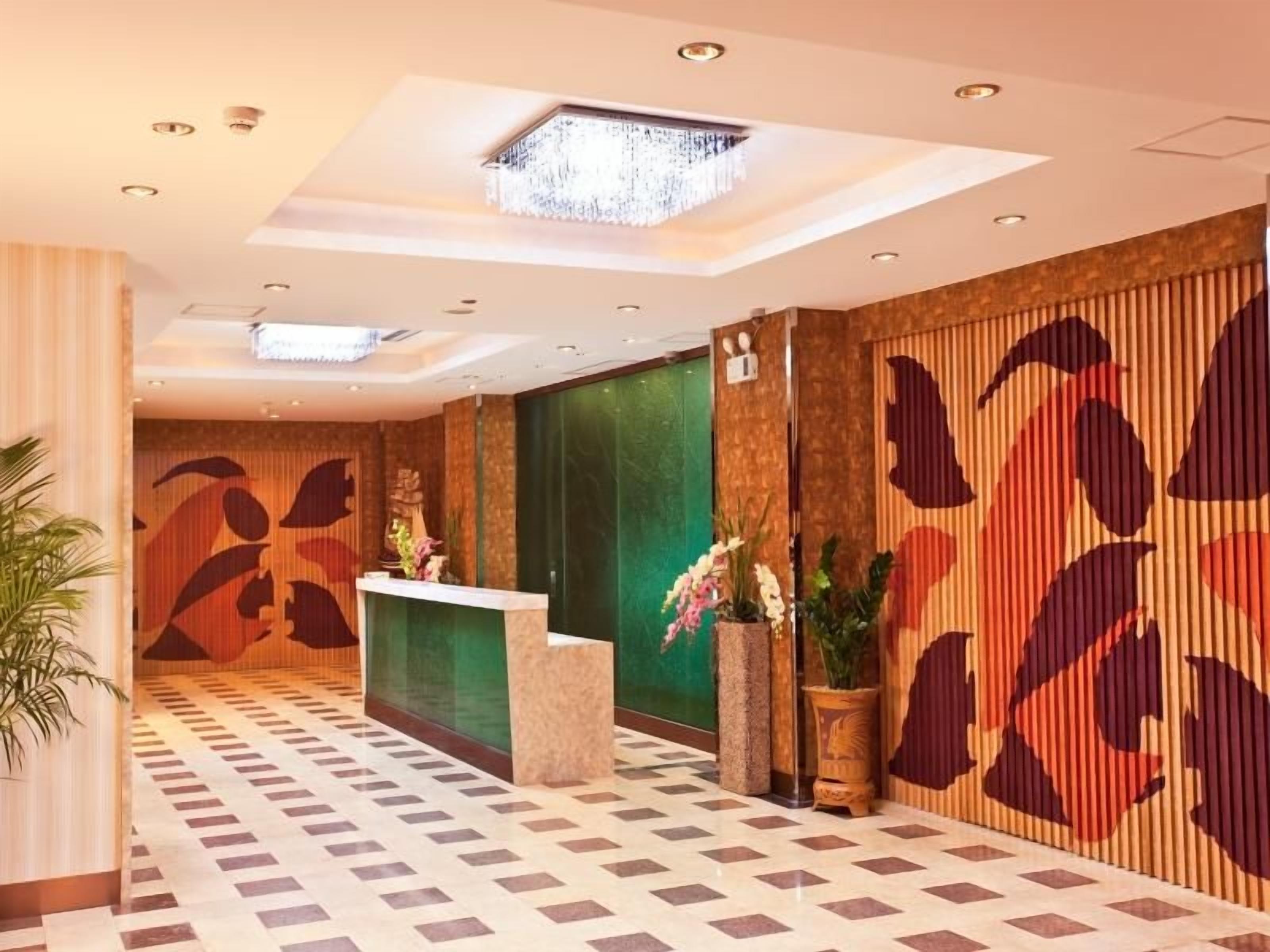 A reception area with a reception desk, potted plants, and a patterned wall.