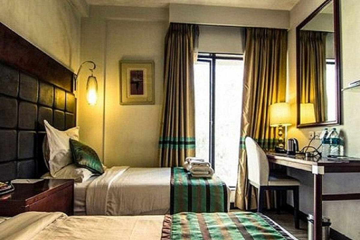 A hotel room with a bed, a desk, a chair, a lamp, and a window with curtains.