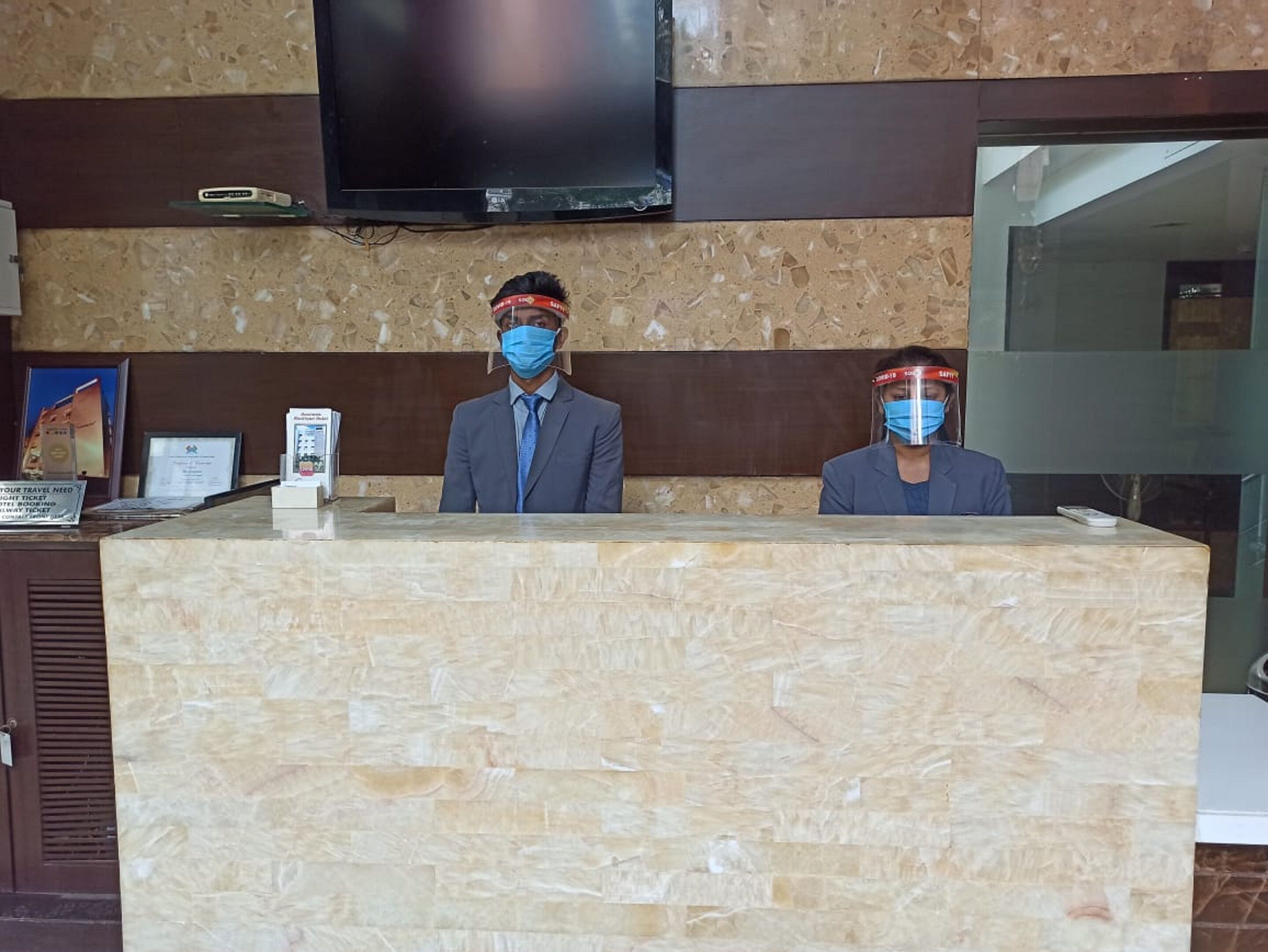 Un mostrador de recepción con encimera de mármol, un televisor de pantalla plana montado arriba y un cartel de bienvenida enmarcado.