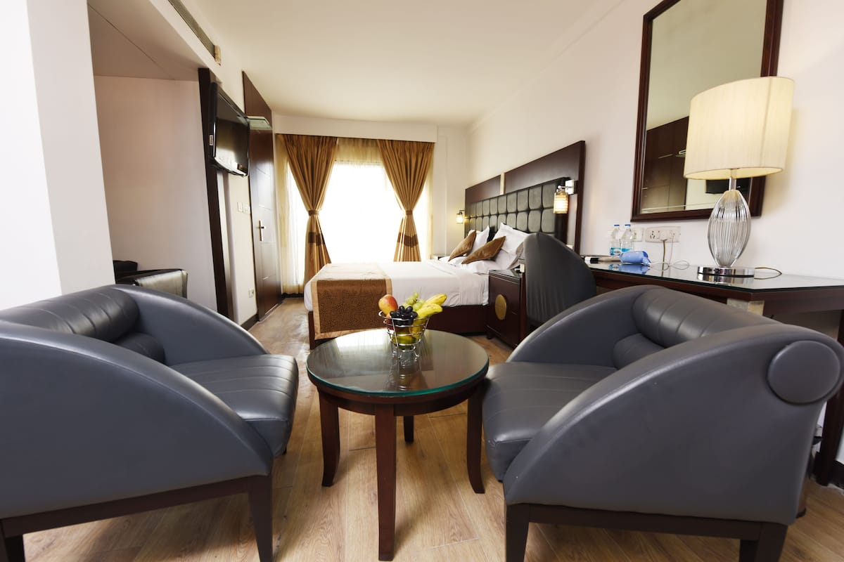 A hotel room with a bed, two armchairs, a small table with fruit, a lamp, and a mirror.