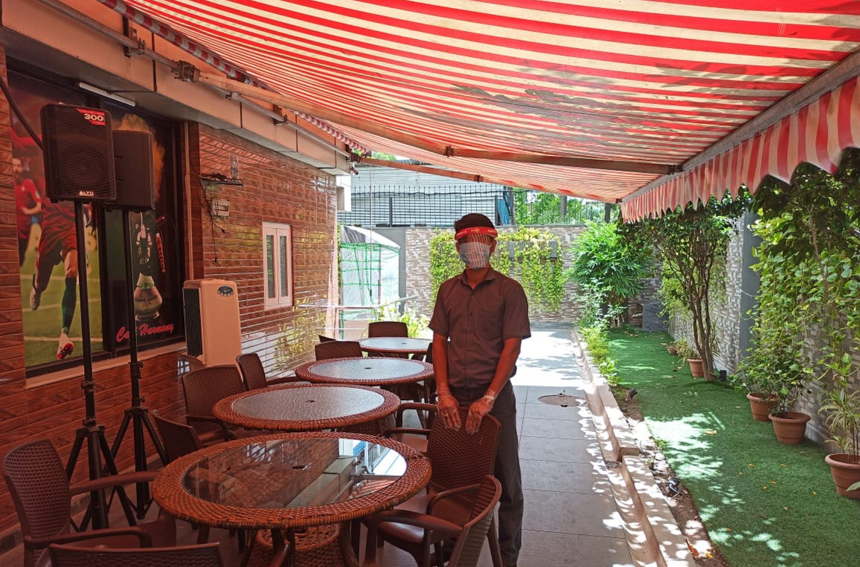 Een terras buiten met ronde tafels en stoelen, een bakstenen muur en potplanten.