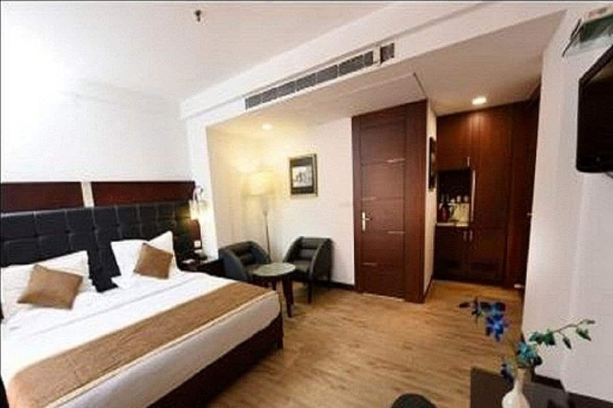 A hotel room with a large bed, a desk, two chairs, a small table, and a wardrobe.
