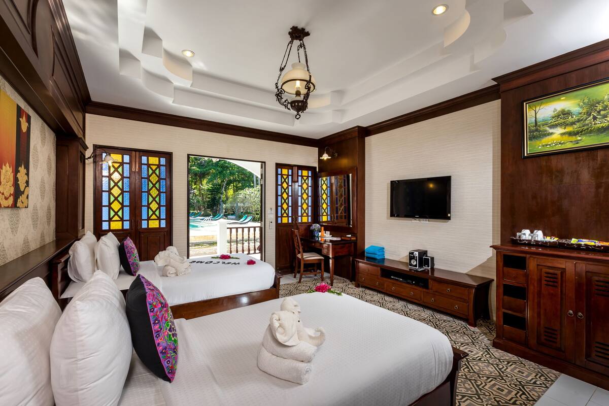A hotel room with two beds, a desk, a TV, and a view of the outdoors.