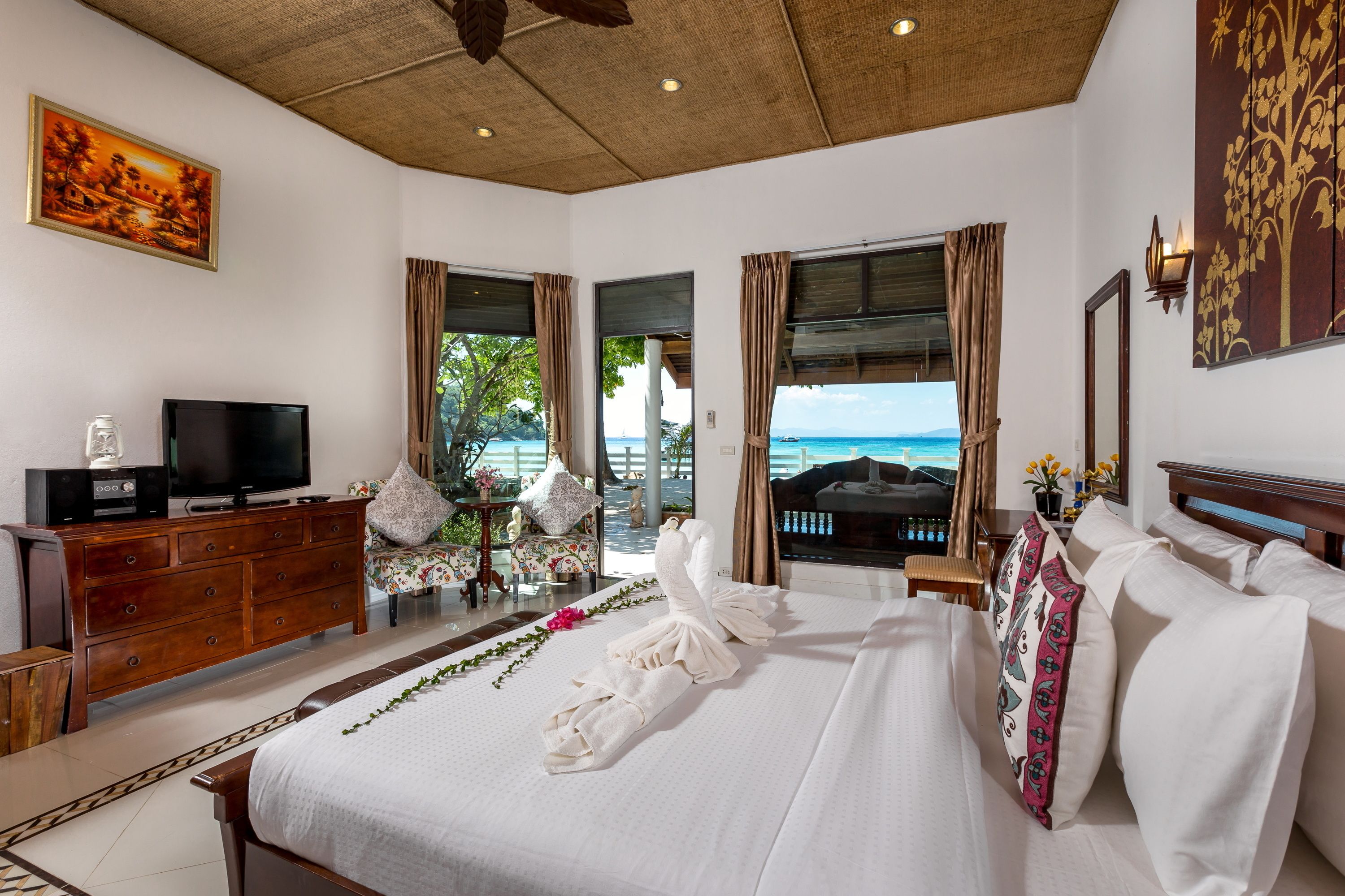 A hotel room with a bed, a TV, a wooden dresser, and a view of the ocean.