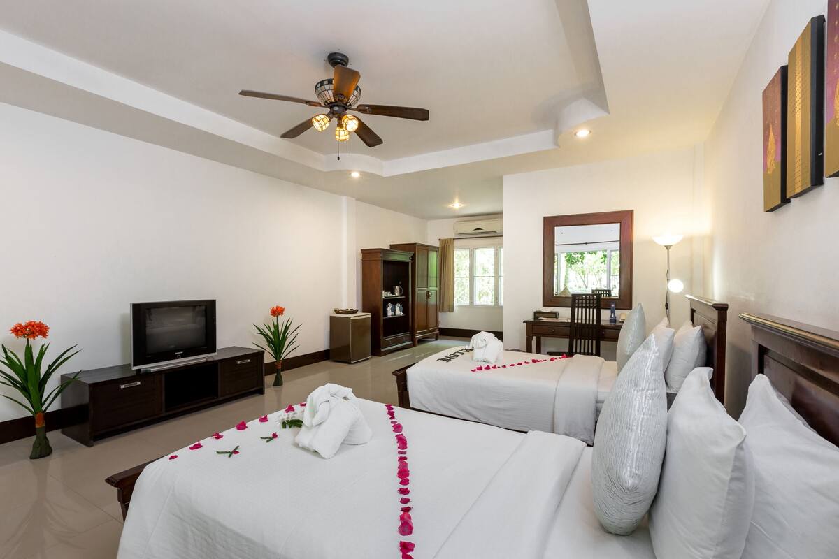 A hotel room with two beds, a TV, a ceiling fan, a desk, and a chair.