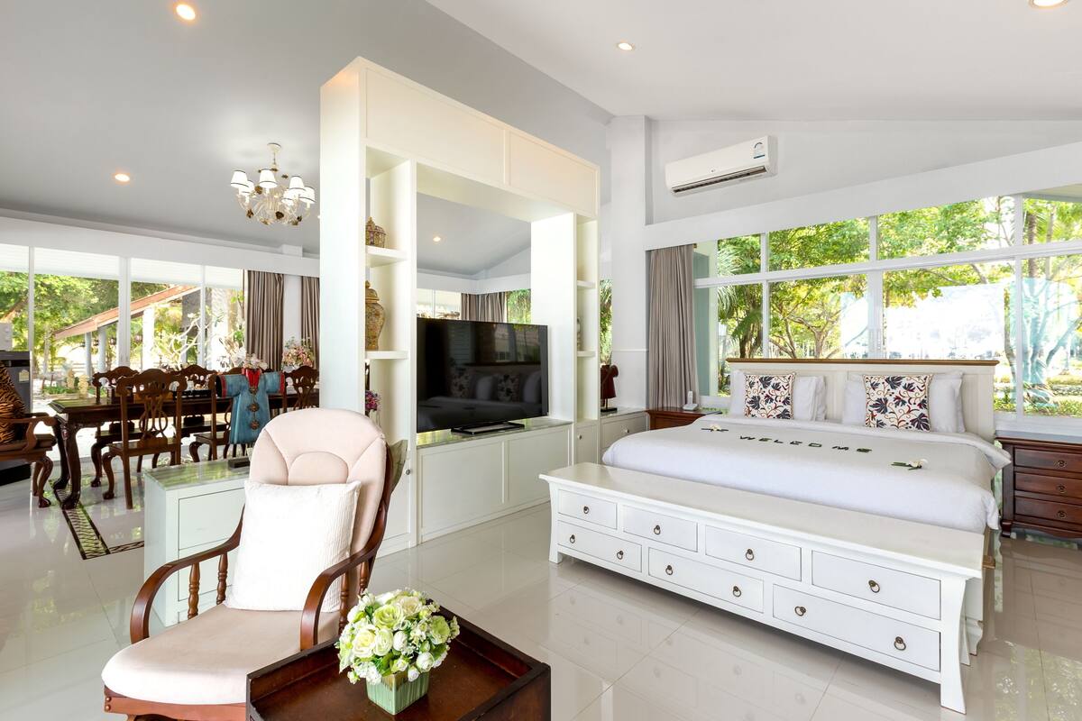 A spacious bedroom with a large bed, a TV, and a dining area with wooden furniture.
