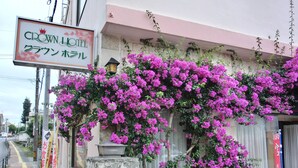 A hotel with a sign in both English and Japanese, surrounded by vibrant pink bougainvillea. - Crown Hotel Okinawa (Okinawa)