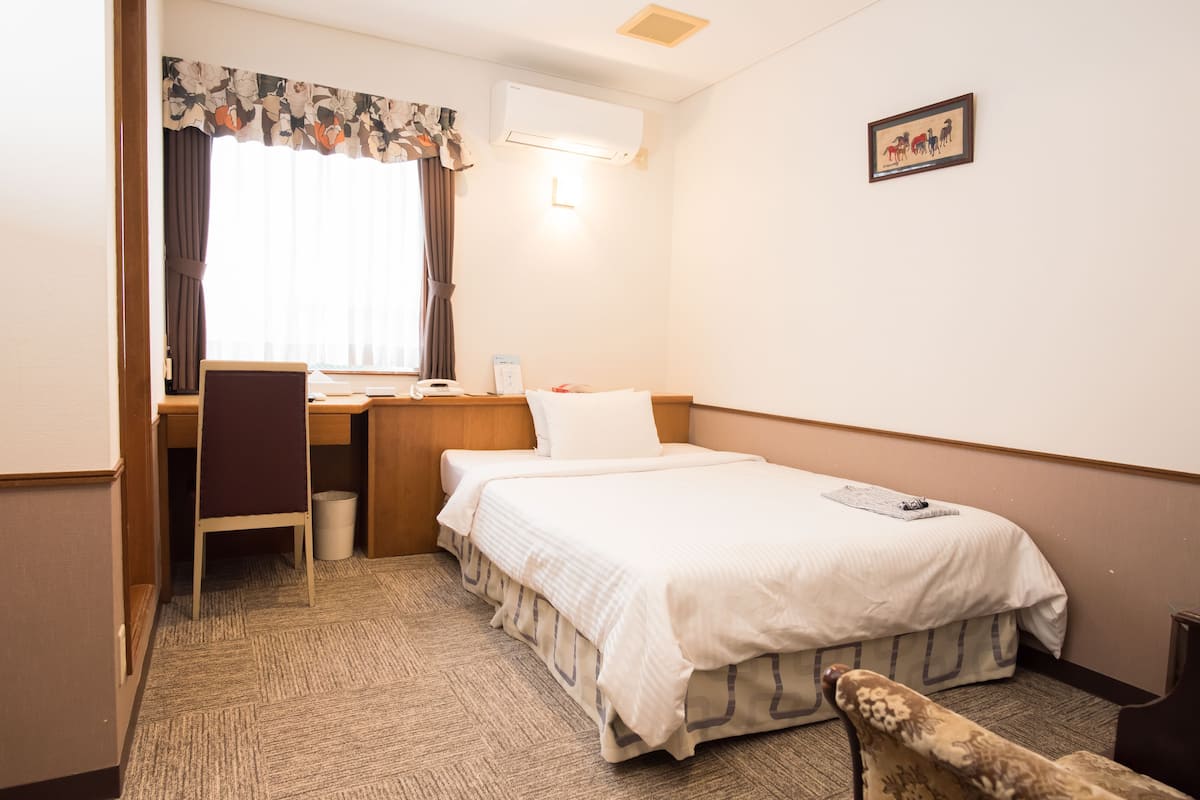 A hotel room with a bed, desk, chair, and a small table.