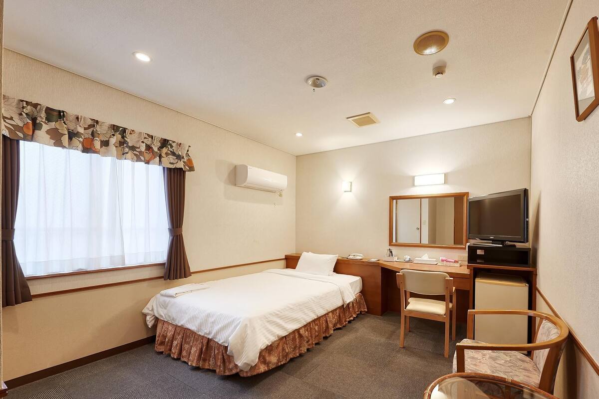 A hotel room with a bed, desk, chair, television, and a window with curtains.