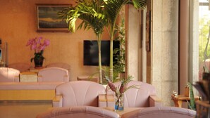 A lobby with leather sofas, a small table with a vase of flowers, a television, and a large window. - Crown Hotel Okinawa (Okinawa)