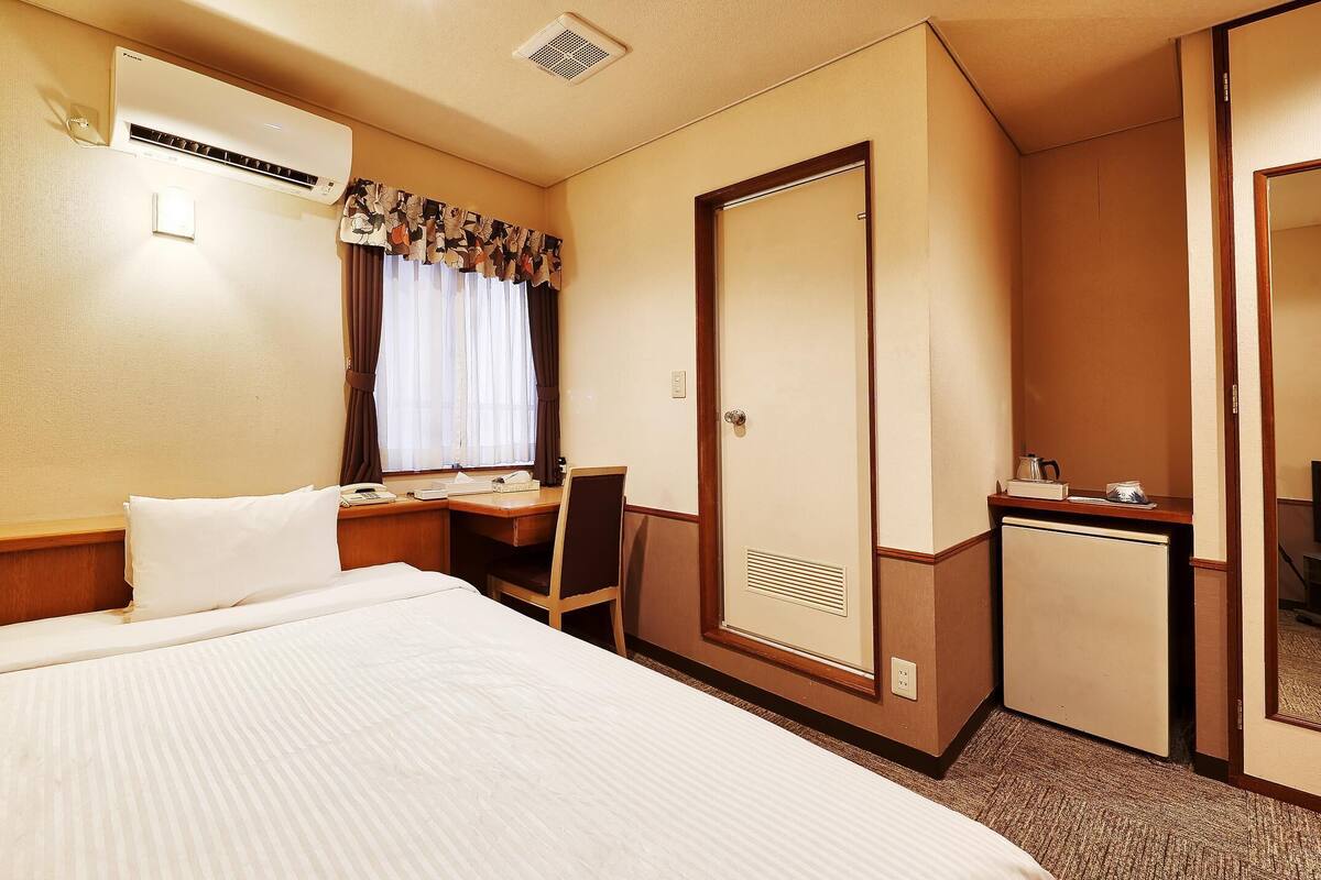 A hotel room with a bed, a desk, a chair, a wardrobe, and a television.