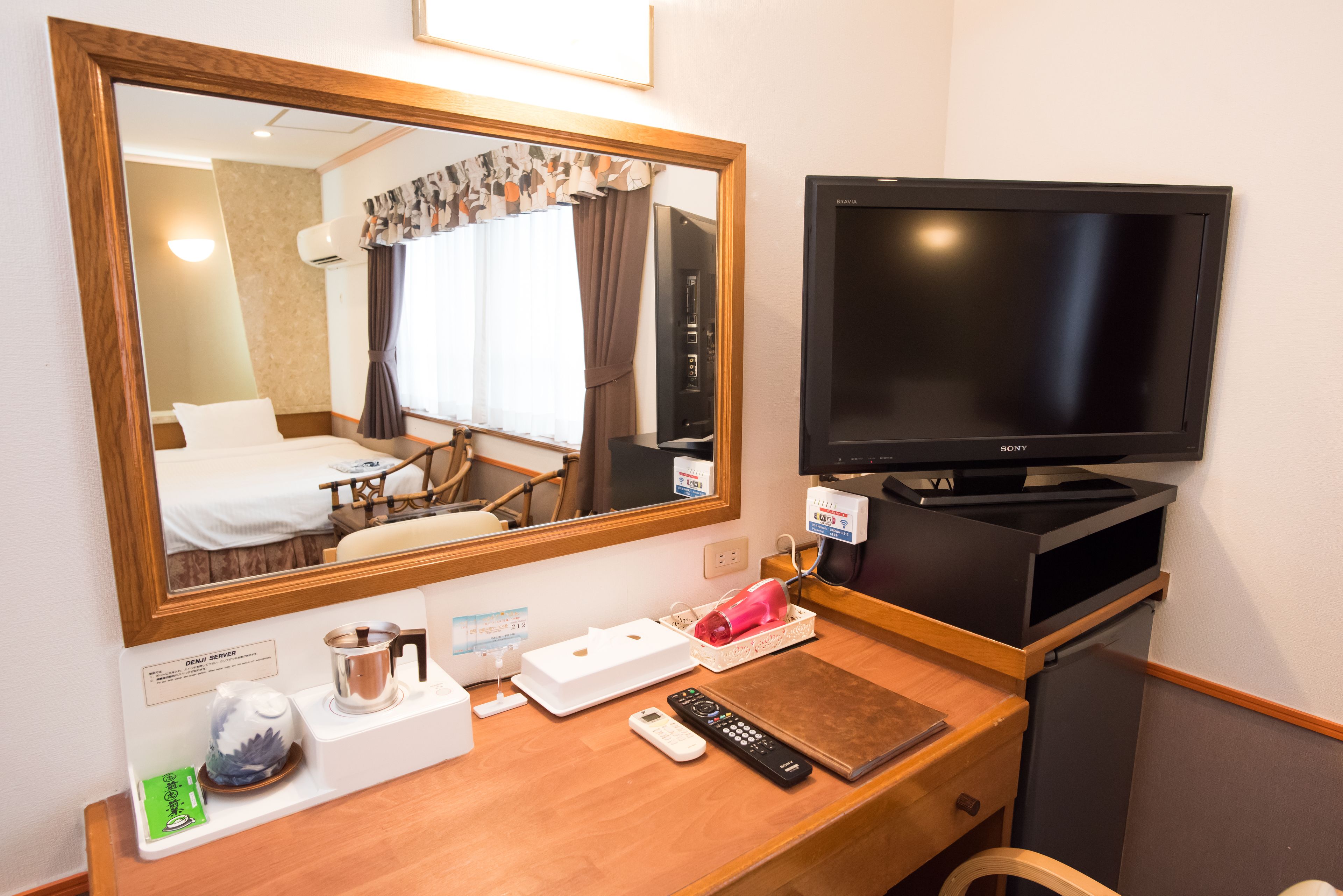 Ein Hotelzimmer mit einem Holztisch, einem Fernseher, einem Spiegel und einem Bett.