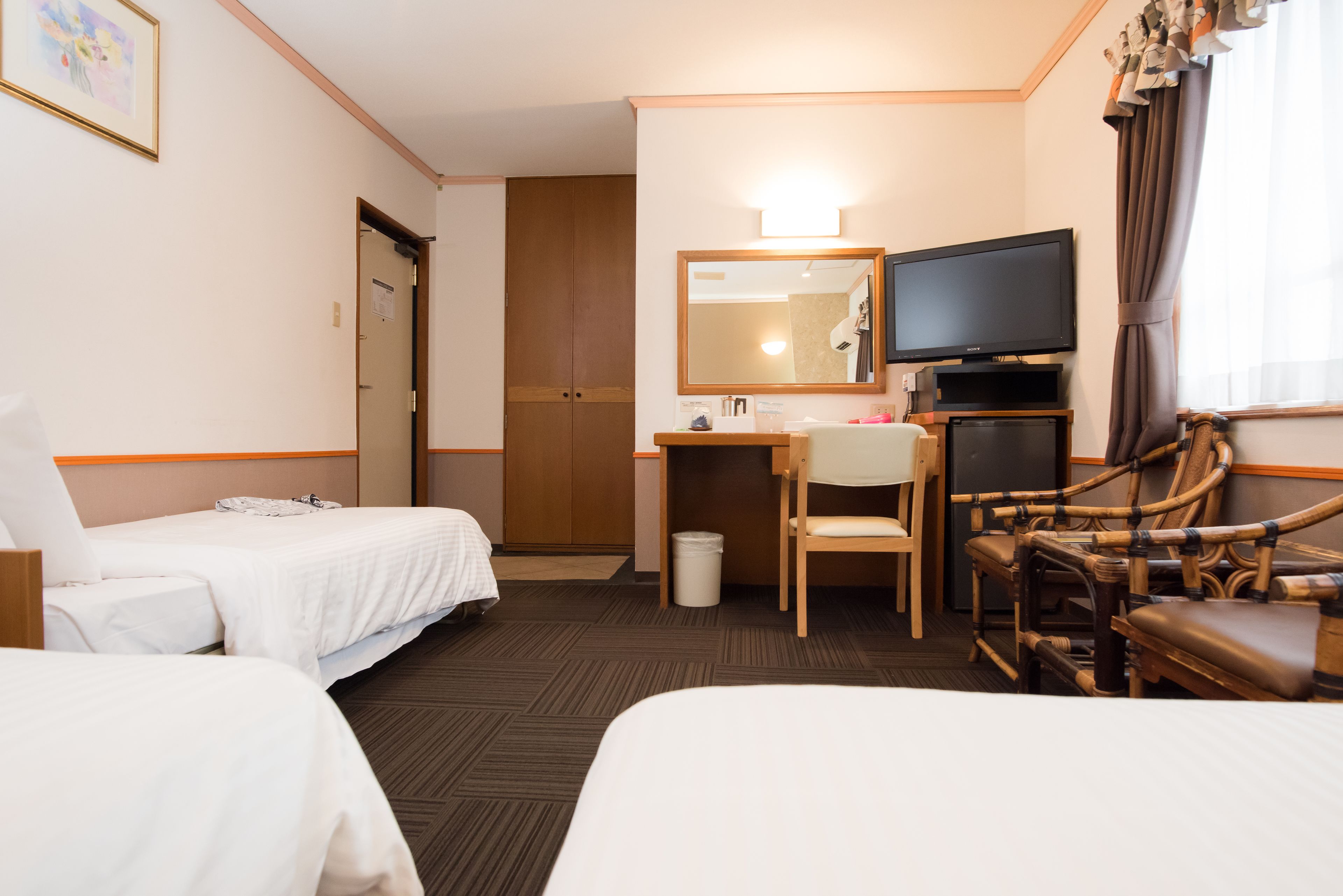 A hotel room with two beds, a desk with a chair, a television, and a large mirror.