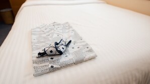 A neatly made bed with a patterned blanket and a pair of headphones on it. - Crown Hotel Okinawa (Okinawa)