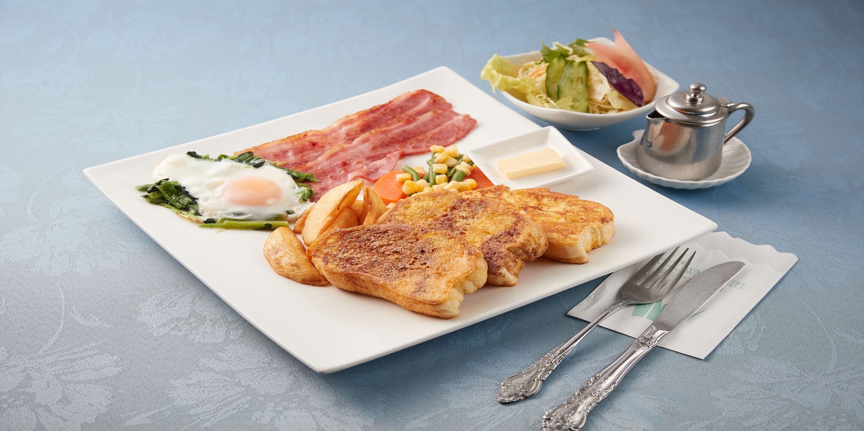 A breakfast plate with bacon, eggs, toast, vegetables, and a side salad.